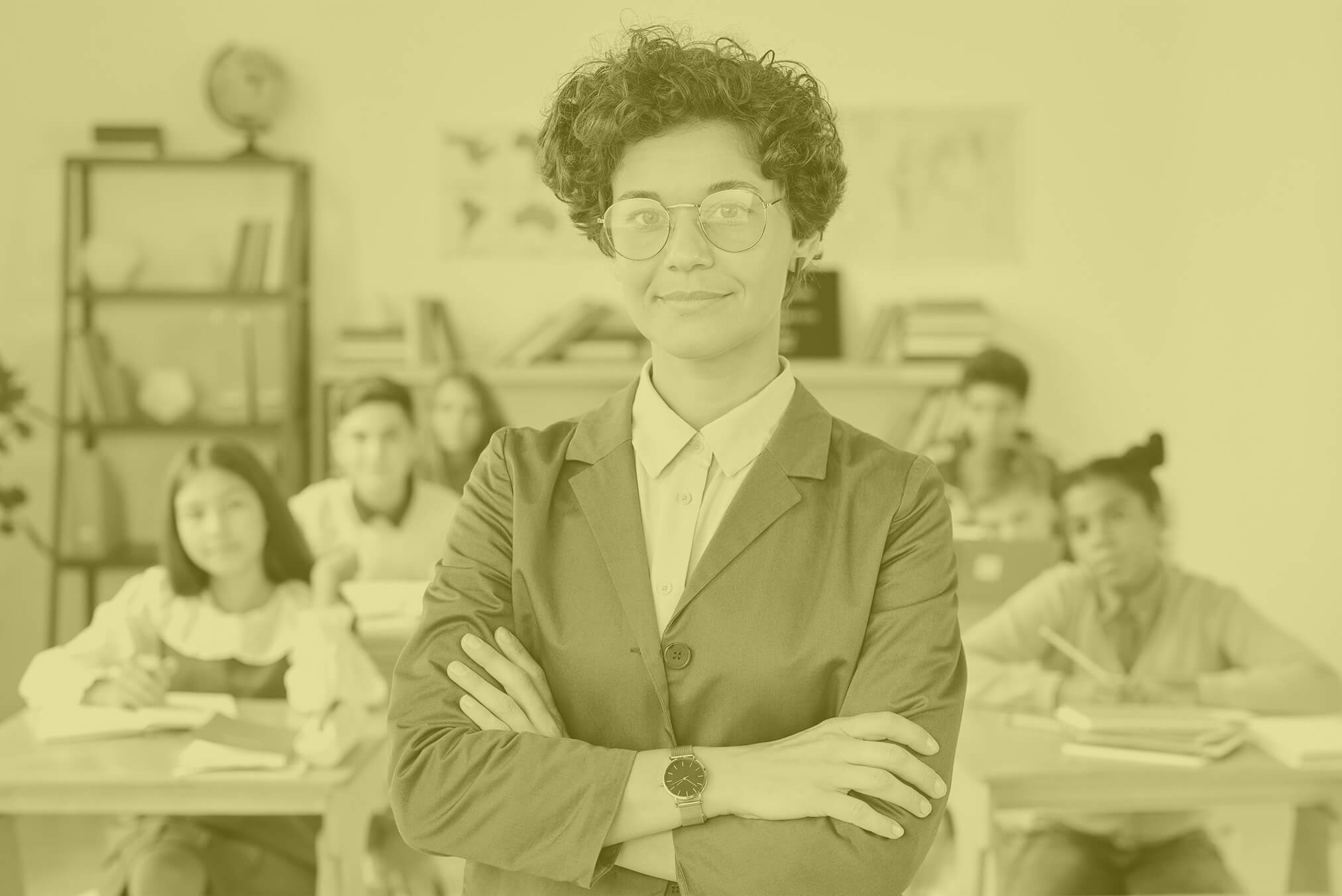 Eine Lehrerin steht lächelnd und mit verschränkten Armen vor Schülerinnen und Schülern in einem Klassenzimmer.