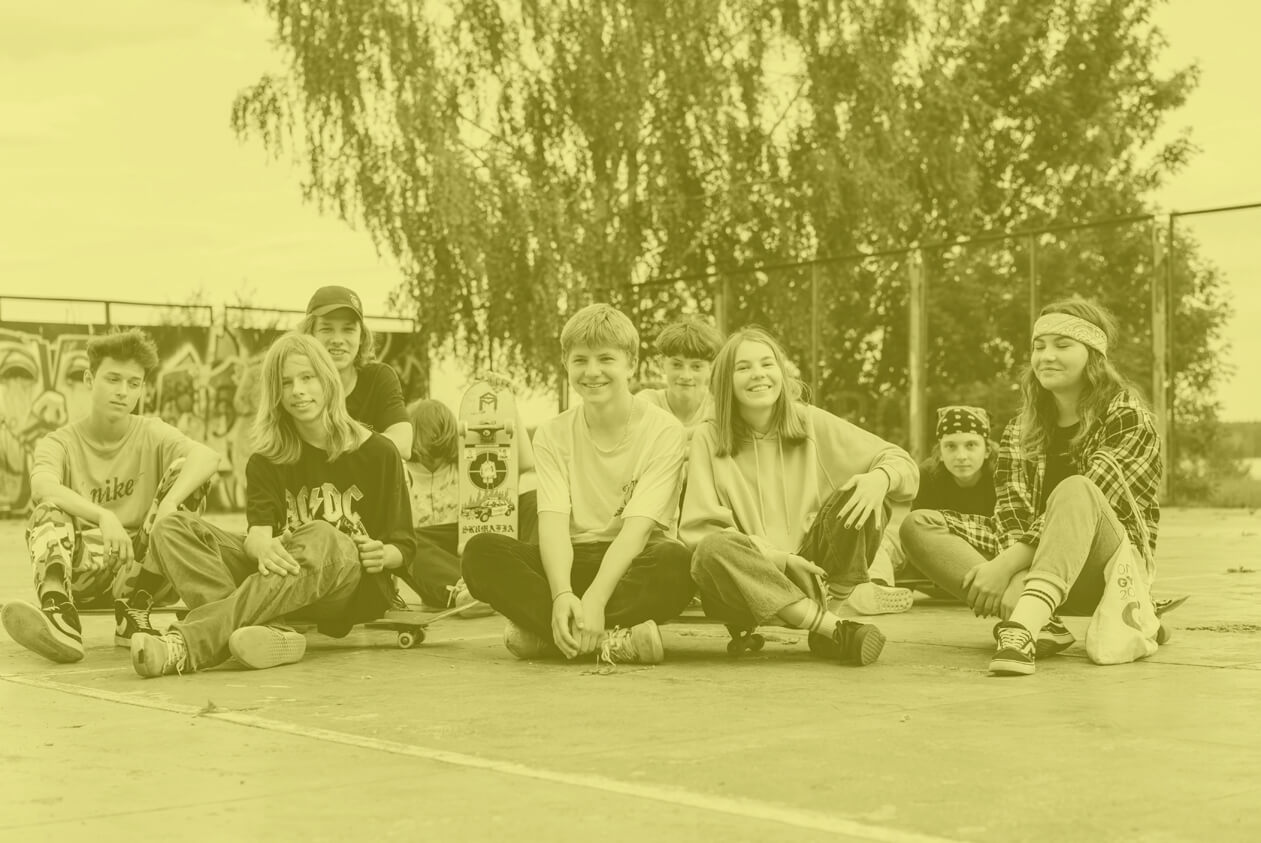 A group of young students sits on a sports pitch.